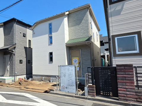 白を基調とした外観に異なる外壁デザインを組み合わせ、街並みに調和しながらも存在感のある佇まいです。前面道路からの視認性も良く、戸建住宅が並ぶ落ち着いた住環境に位置しています。
