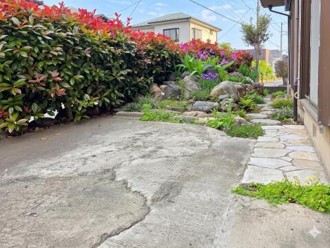 敷地内にはコンクリート部分と植栽スペースが確保されており、駐車スペースとしての利用や庭としての使い分けができる配置です。外構には石組みや植栽が施され、戸建ならではのゆとりある空間が広がっています