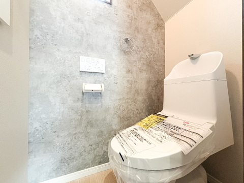 グレーのアクセントクロスが落ち着いた雰囲気を醸し出す、こだわりのトイレ空間。毎日使う場所だからこそ、デザイン性にもこだわり、心地よい清潔感を演出しています。