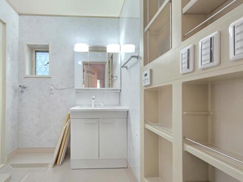 洗面室には三面鏡付きの洗面化粧台を備え、身支度に必要な小物をすっきり収納できます。壁面には豊富な収納棚を設け、タオルや洗剤なども整理しやすく、窓から換気もできる使い勝手の良い空間です。