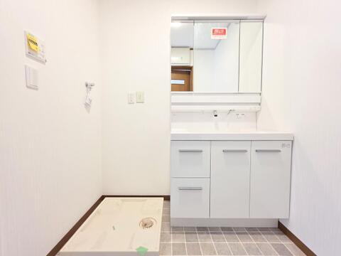 新規交換された洗面化粧台は、三面鏡と収納を備えた使いやすい仕様です。洗面用品をすっきり整理でき、広い洗面ボウルで毎日の身支度も快適です。洗濯機置場も隣接し、家事動線に配慮された清潔感のある洗面室です。