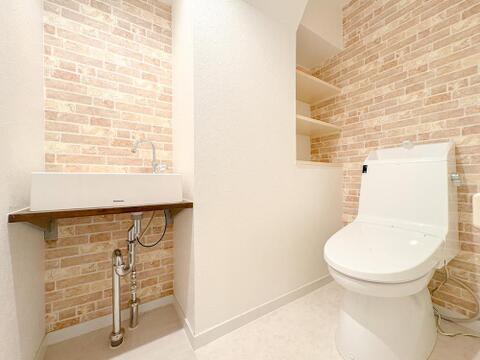 おしゃれなレンガ調の壁紙が印象的なトイレ空間です。手洗い器と収納棚も完備しており、清潔感と機能性を両立。家族みんなが快適に使えるデザインです。