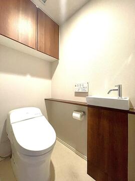 木目調の収納と手洗い器がスタイリッシュなトイレ空間。温水洗浄便座で快適、上部収納でストックもすっきり片付き、いつも清潔に保てます。