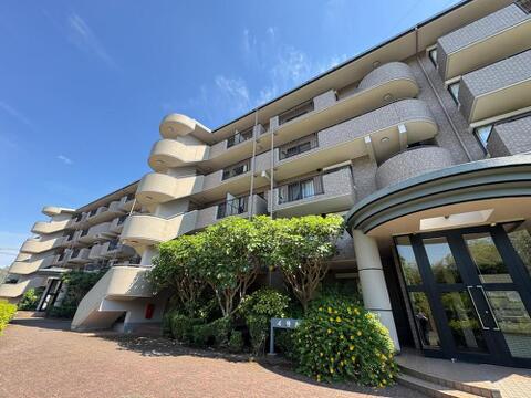 青空に映える、洗練されたデザインのマンション外観です。手入れの行き届いた植栽が、日々の暮らしに彩りを添え、家族の笑顔が溢れる明るい毎日を演出します。