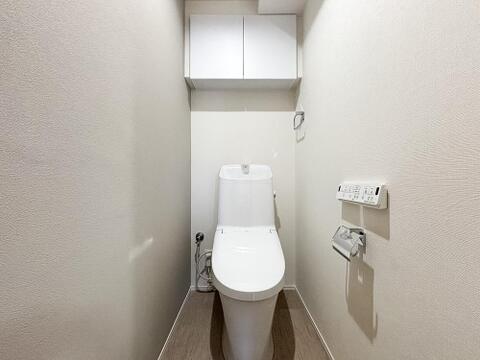 白を基調とした清潔感のあるトイレ。温水洗浄便座や壁付けのリモコンなど、機能面も充実しています。上部には扉付きの吊戸棚があり、ストック類を隠してスッキリ収納可能です。