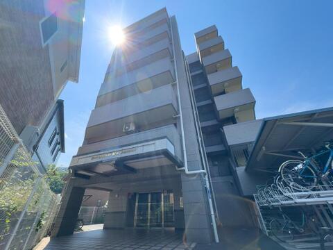 晴れ渡る青空の下、陽光が降り注ぐマンション外観。広々としたエントランスと便利な駐輪場で、快適な毎日を。