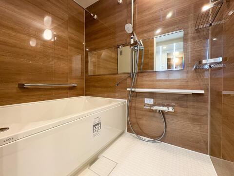 高級感ある木目調パネルのバスルーム。横型ミラーや手すり、便利な棚も備わった快適な癒やし空間。