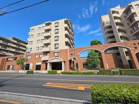 重厚感のあるタイル貼りの外観とアーチ形のエントランスが印象的なマンションです。手入れの行き届いた植栽が街並みに彩りを添え、ゆとりある敷地計画が落ち着いた住環境を演出します。