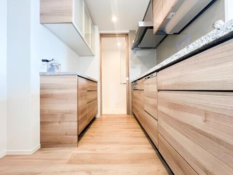 木目デザインが洗練されたシステムキッチン。背面には調理家電や食器を効率よく収納できるカップボードを設置。機能的で作業スペースも広々とした快適空間です。