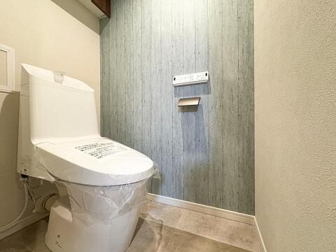 温水洗浄機能付きの快適なレストルーム。おしゃれなアクセント壁に加え、上部にはトイレットペーパーなどを隠してすっきり収納できる便利な吊戸棚を備えています。