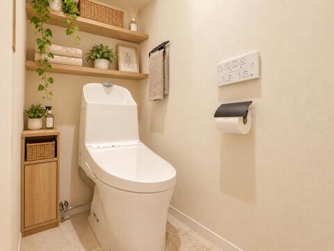 白を基調とした温水洗浄便座採用のトイレ。トイレットペーパーや清掃用品を置ける上部棚と足元キャビネットを備え、限られたスペースを有効活用した造りになっています。※家具はCG加工です。