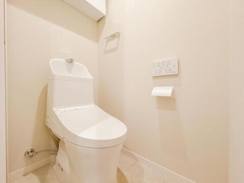 全体をホワイトでまとめた清潔感のあるトイレ空間です。壁掛け式のリモコンや上部吊戸棚を設置しており、トイレットペーパーや清掃用品をスッキリと収納しておくことができます。