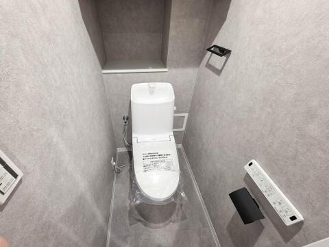 トイレは温水洗浄便座付きの設備に交換済みです。壁付けリモコンで操作しやすく、タンク上には手洗い器を備えています。背面の棚には芳香剤や小物を置けるため、床に物を増やさず、空間をすっきりと使えます。