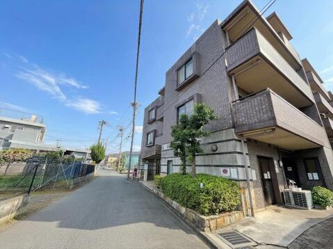建物の外壁はタイル張りで、窓周りの縁取りやバルコニーの形状が外観のアクセントになっています。道路沿いには石張りの植栽スペースを設けています。共用玄関にはオートロックを備えたマンションです。