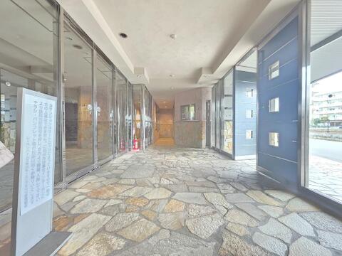 エントランスは床や壁の一部に石張りを施し、ガラス面から外の光が入る造りです。天井にはダウンライトを配し、奥には管理室の窓口を設けています。共用玄関のオートロックで来訪者の入館を管理します。