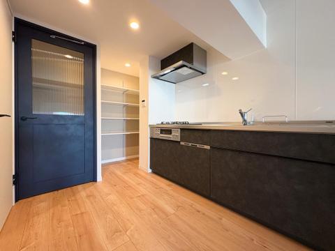 黒の意匠が光るキッチン。奥には可動棚のパントリーを備え、デザイン性と収納力を高い次元で両立。