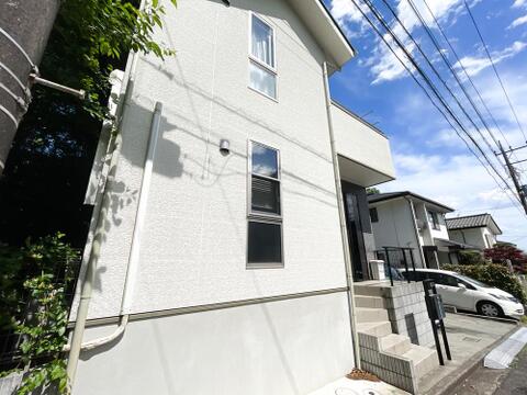 青空に映える、白とグレーのスタイリッシュな邸宅。洗練されたモノトーンのデザインに、背景の鮮やかな緑が美しく調和します。高台に位置し、開放感あふれる空を独り占めできる、デザイナーズ住宅のような佇まいが