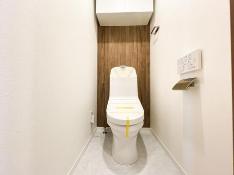 深みのある木目調のアクセントクロスが、ホテルのような落ち着きを醸し出すトイレ空間。毎日を快適に過ごせるリモコン付きの温水洗浄便座を採用しています。上部にはトイレットペーパーのストックに便利な吊戸棚付き