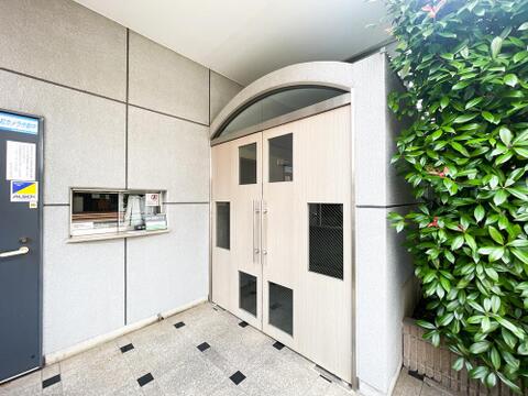 木目調の扉と緑の植栽が彩る上品なアプローチ。安心のオートロック・管理室窓口付き。