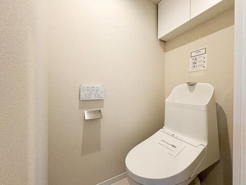 白を基調とした清潔感のあるトイレ空間。便利な壁掛けリモコンタイプの温水洗浄便座を採用しています。上部には吊り戸棚を備え、ペーパー等の備品もスッキリ収納可能です。