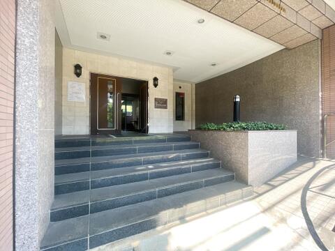 大理石調の壁面がゲストを優雅に出迎えるエントランスアプローチ。重厚な扉の横には植栽スペースが配されており、階段に加えてフラットなスロープも併設された、優しいユニバーサル設計です。