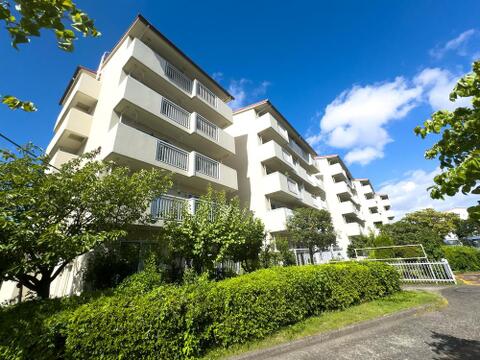 爽やかな青空の下、緑豊かな植栽に彩られたマンション。明るいバルコニーが心地よい風を運び、家族の毎日を優しく包み込みます。穏やかな環境で子育てを。