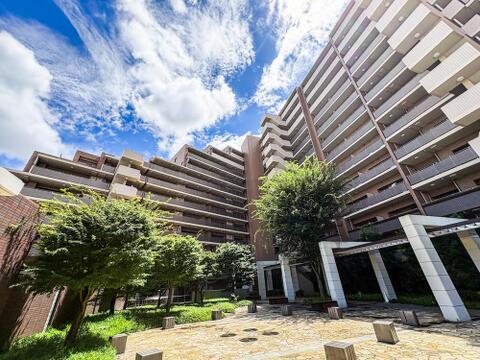青空の下、緑豊かな広場が広がるマンション外観。お子様がのびのびと遊べるスペースがあり、家族の笑顔が溢れる毎日を育みます。