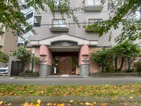 ピンクベージュの柱と緑豊かな植栽が調和する、温かみと高級感を兼ね備えたエントランス。