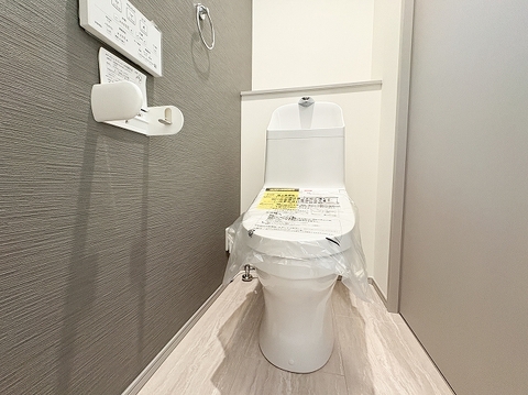ダークグレーのアクセントクロスがおしゃれで落ち着いた雰囲気を演出するレストルーム。手洗い付きの温水洗浄便座を完備し、奥の棚には小物も飾れる快適で清潔感あふれる空間です。