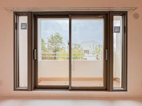 リビングの大きな窓からバルコニー方向を望む一枚。窓の先には樹木や空が見え、室内にいながら屋外の景色を身近に感じられます。
