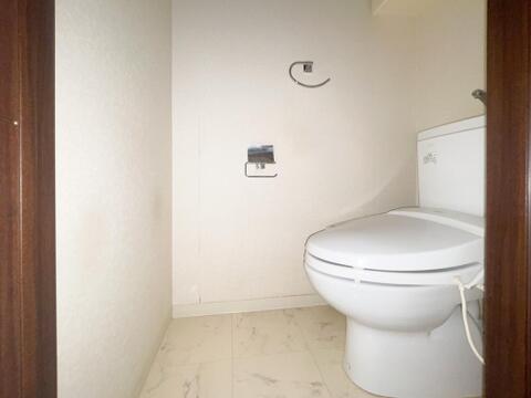 トイレの床には、大理石調のタイルが採用されており、清潔感のある空間となっています。壁面にはペーパーホルダーやタオル掛けがシンプルに配置された、すっきりとした造りです。