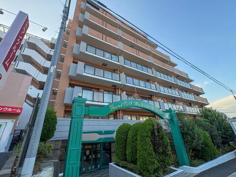 「Grand City Hachioji Kitao」のモダンな外観。緑に囲まれたエントランスが、家族の笑顔を育む毎日を演出します。
