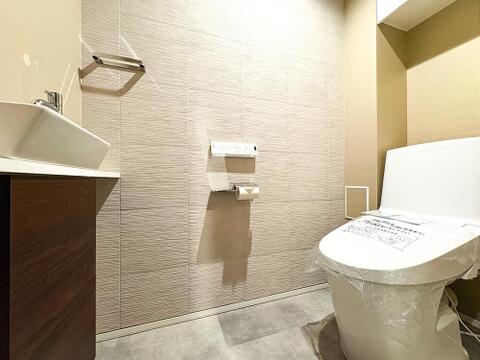 質感豊かなアクセントクロスとシックなフロアタイルが調和する上質なレストルーム。最新の温水洗浄便座や手洗い場を備え、毎日のお手入れもしやすい衛生的な設計です。