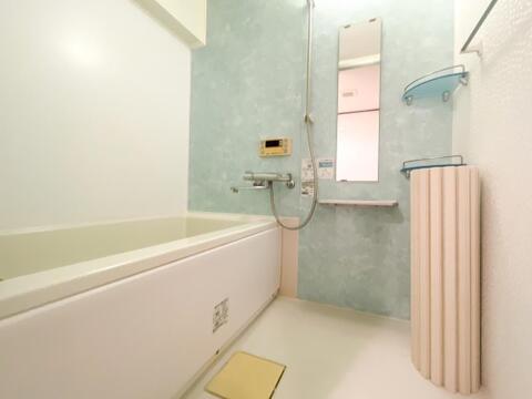 水色系のアクセントパネルが爽やかな印象を与える浴室です。縦長の鏡やシャンプーなどの小物を置けるラックが備わっており、使い勝手に配慮されています。お湯張りに便利なリモコンも設置されています。
