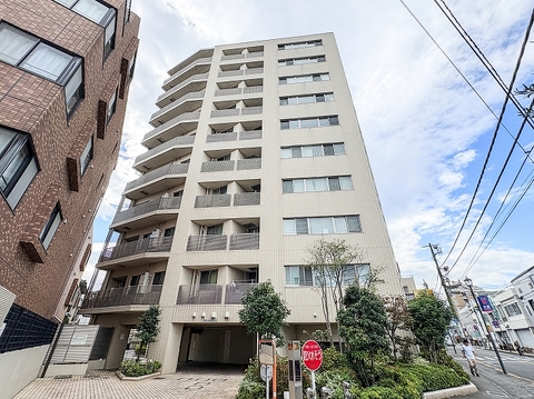 建物の足元をぐるりと囲む豊かな低木・高木のグリーンが、道路とマンションを優しく調和。人工構造物の硬さを和らげ、まるで緑の庭園から建物が立ち上がっているかのような潤いある街並みを形成しています。