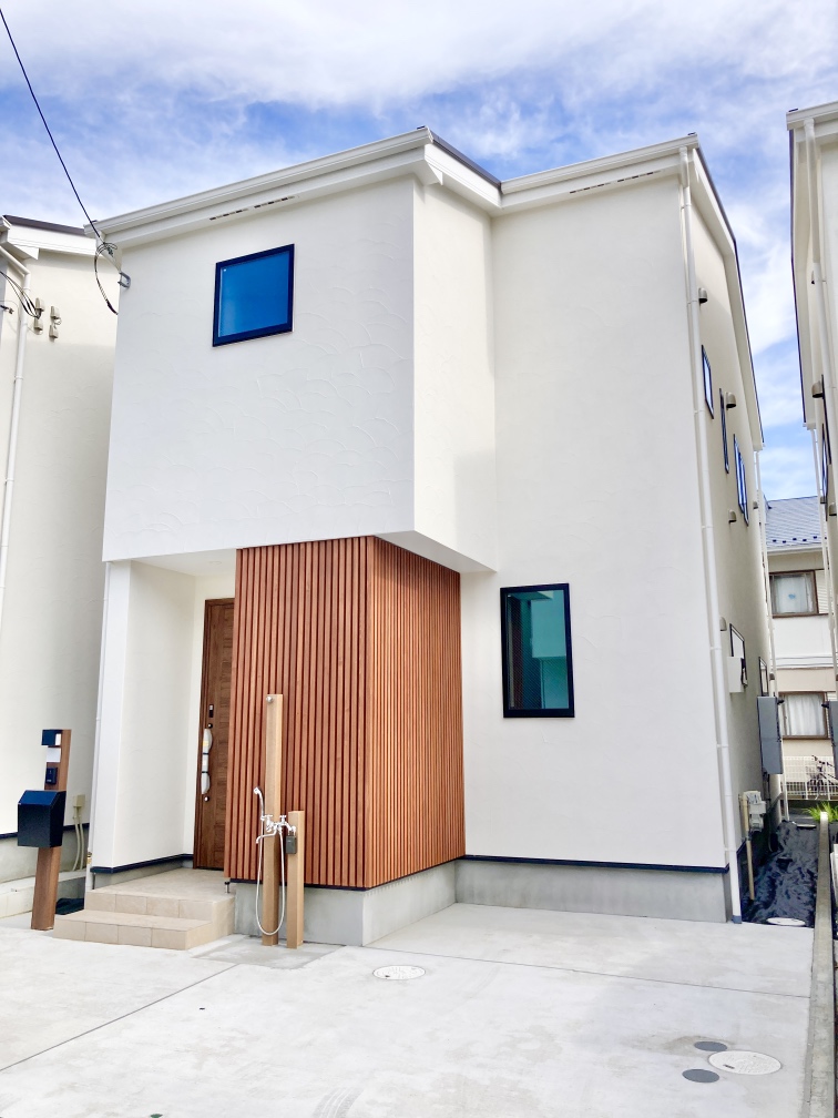 【現地外観写真】白い外壁が青空に映える、1LDK+2Nの住まい。家事負担を軽減する便利な設備が搭載されています。小学校まで徒歩3分、スーパーまで徒歩8分の立地です。