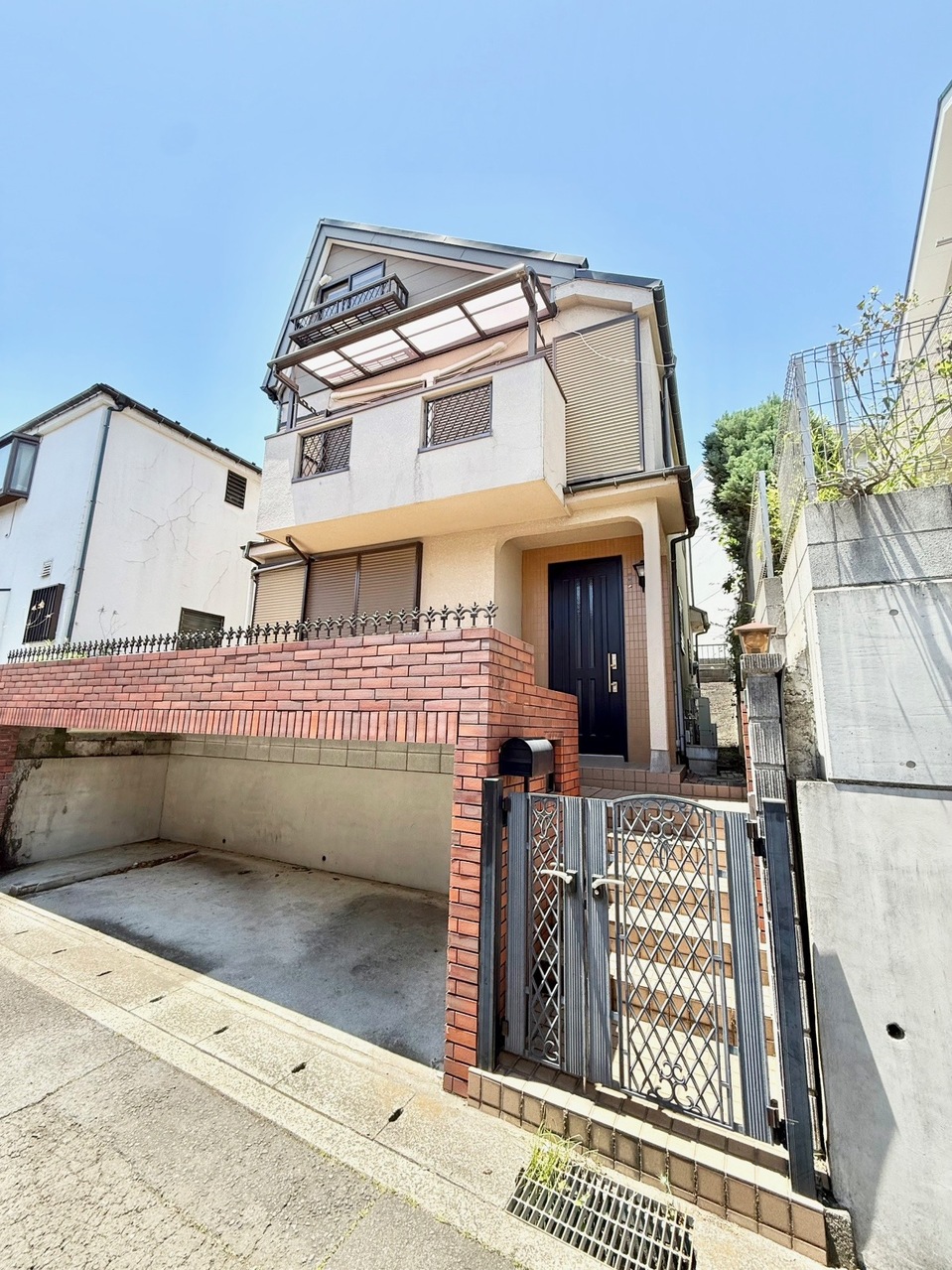 【現地外観写真】陽光が心地よく注ぐタイルテラスが設けられた住まい。屋根と壁のある駐車スペースも設けられており、愛車を雨風から守ることができます(車種制限有)。