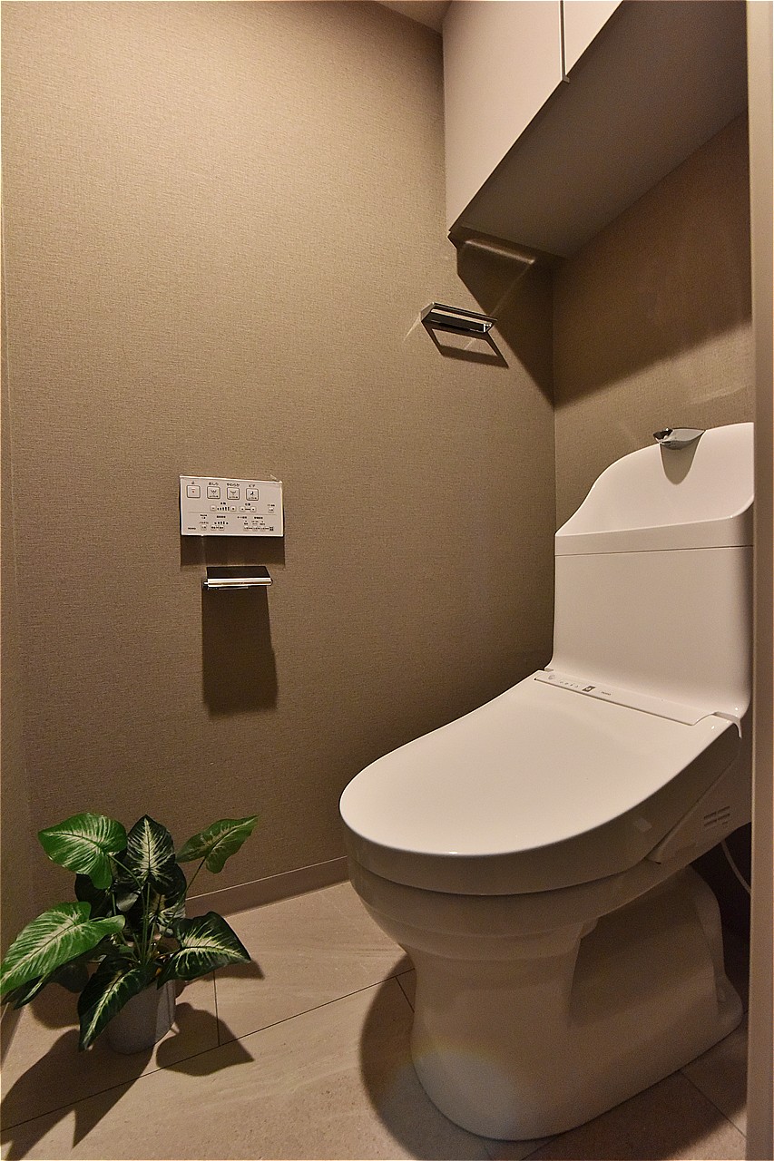 温水洗浄便座付きのトイレです。寒い時期でも温かな便座で快適に使うことができます。上部には吊り戸棚があり、トイレットペーパーや掃除用具の収納に便利です。