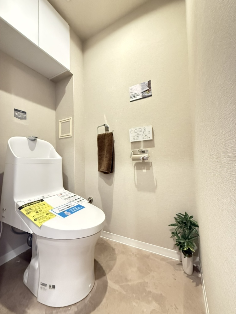 【トイレ】トイレットペーパーのストックや掃除用品などの収納に便利な吊戸棚が設置されています。温水洗浄便座付きで、毎日快適に使用できます。