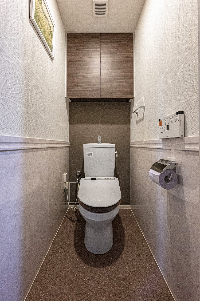 【トイレ】毎日快適にお使いいただける、温水洗浄便座付きのトイレです。背面上部に、トイレットペーパーのストックなどを収納可能な吊戸棚が設置されています。