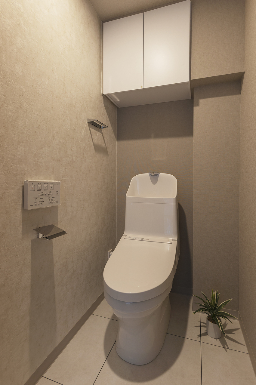 【トイレ】トイレットペーパーのストックや、掃除用品などの収納に便利な吊戸棚を設けています。リモコンは壁に設置しているため、操作がしやすいです。