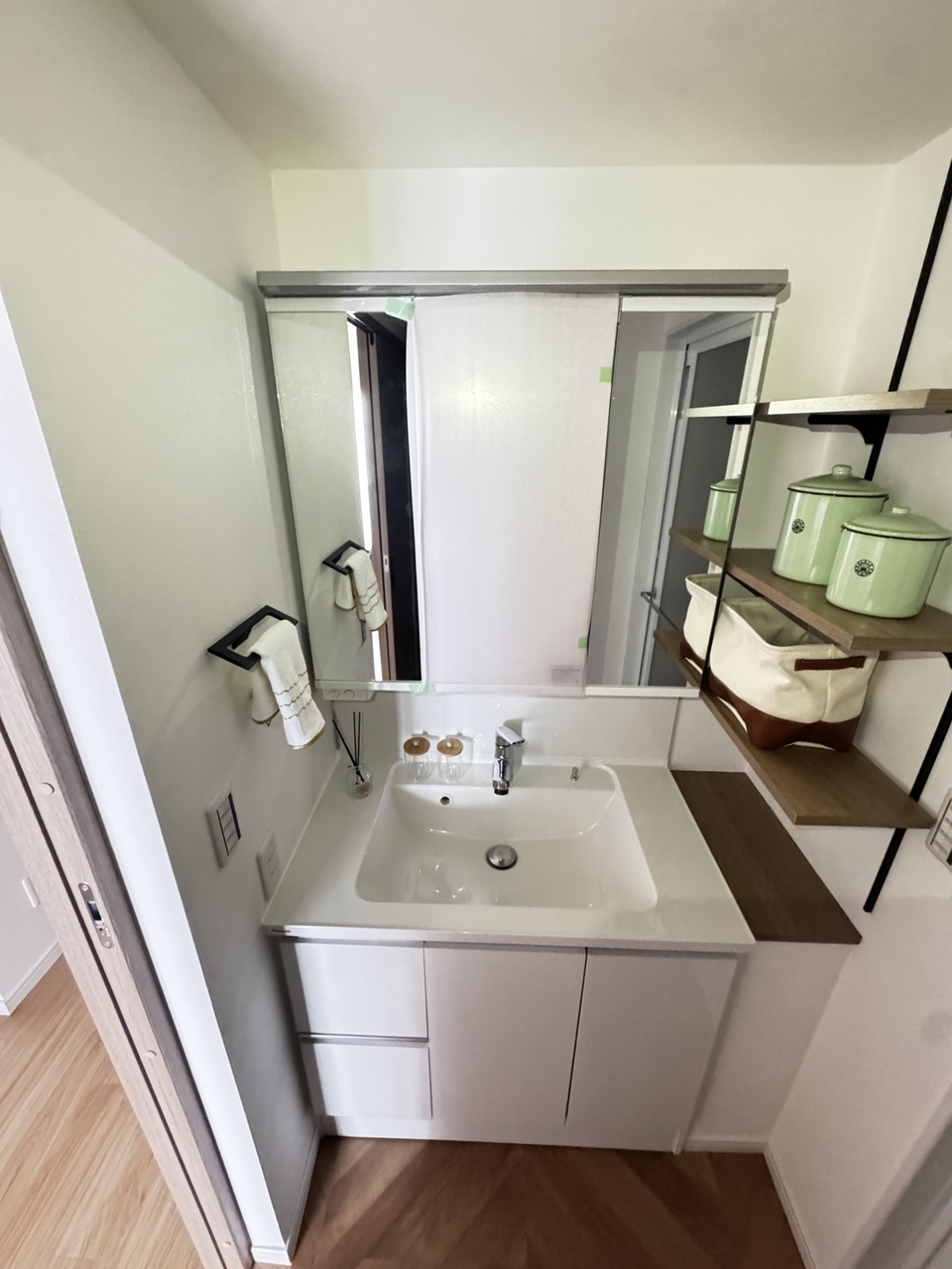 【洗面所】三面鏡付きの洗面化粧台が設置されています。鏡裏・洗面ボウル下に加え、洗面台横に収納が設けられており、日用雑貨を収納可能です。