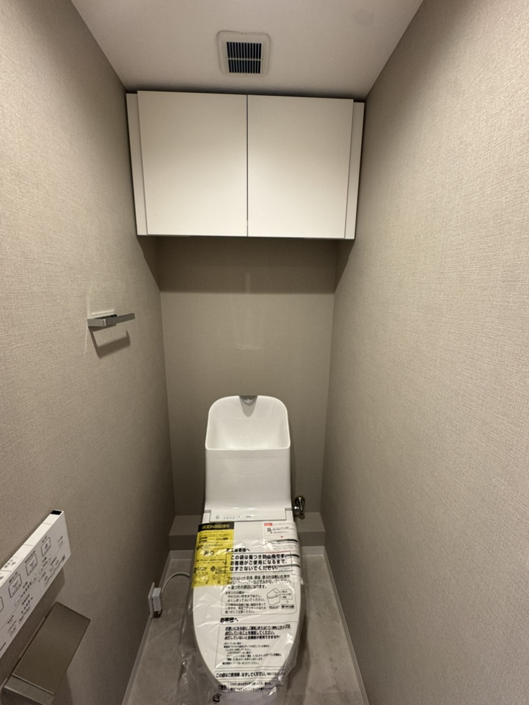 【トイレ】年間を通して、快適に使うことができる温水洗浄便座付きのトイレです。リモコンは操作しやすい壁付けタイプ。上部には吊戸棚が設けられています。