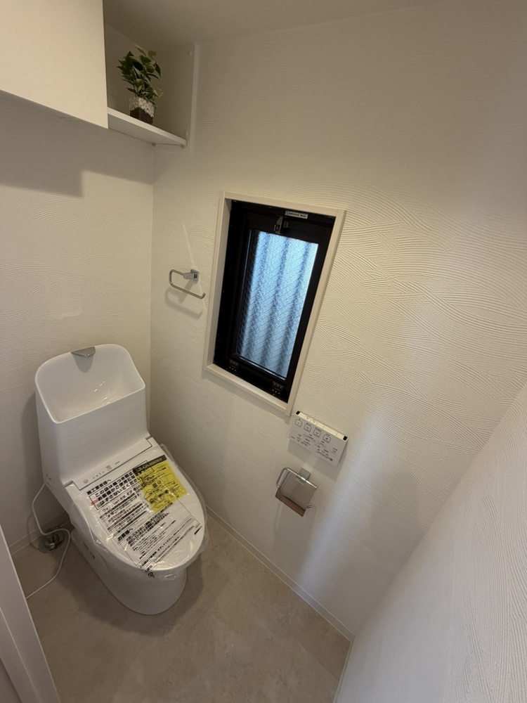 【トイレ】温水洗浄便座付きのトイレが設置されています。上部には吊戸棚があるため、ストック類をすっきりと収納可能。操作リモコンは壁付けのため、操作がスムーズです。