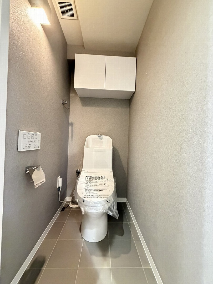 【トイレ】清潔に利用できる温水洗浄機能付きトイレです。上部には収納棚が設置されており、トイレットペーパーや掃除用品を収納することができます。