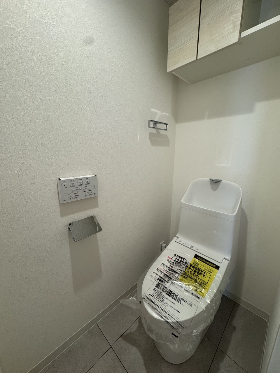 【トイレ】ホワイトを基調としたシンプルな内装です。上部には棚が設置されており、トイレットペーパーや掃除用具などをまとめて収納可能です。