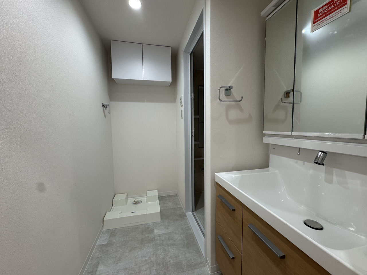 【洗面室】洗濯機置き場には防水パンが設置されており、万が一の水漏れでも被害を最小限に抑えてくれます。上部には、洗剤やバス用品のストックに便利な吊り戸棚があります。