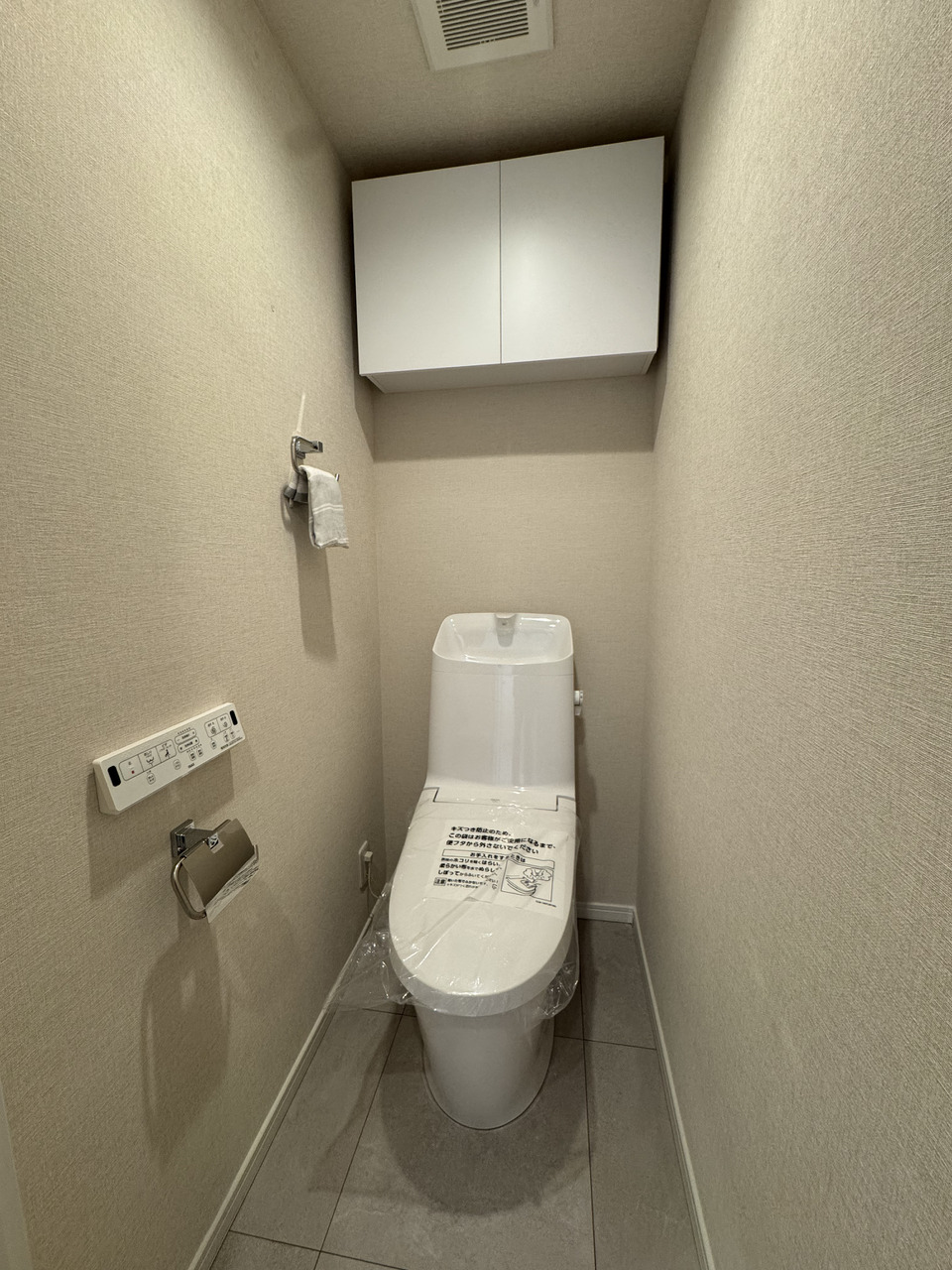 【トイレ】温水洗浄便座のリモコンは壁に取り付けられているので、操作がしやすいです。背面には日用品を収納できる吊戸棚が備わります。