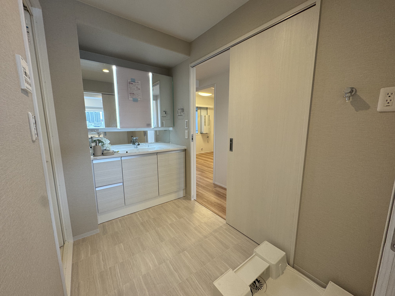 【洗面所】キッチン側・廊下側の2方から出入り可能な、回遊性のある間取り設計。三面鏡付きの洗面化粧台があり、ヘアセットやメイクの際に利用しやすいです。