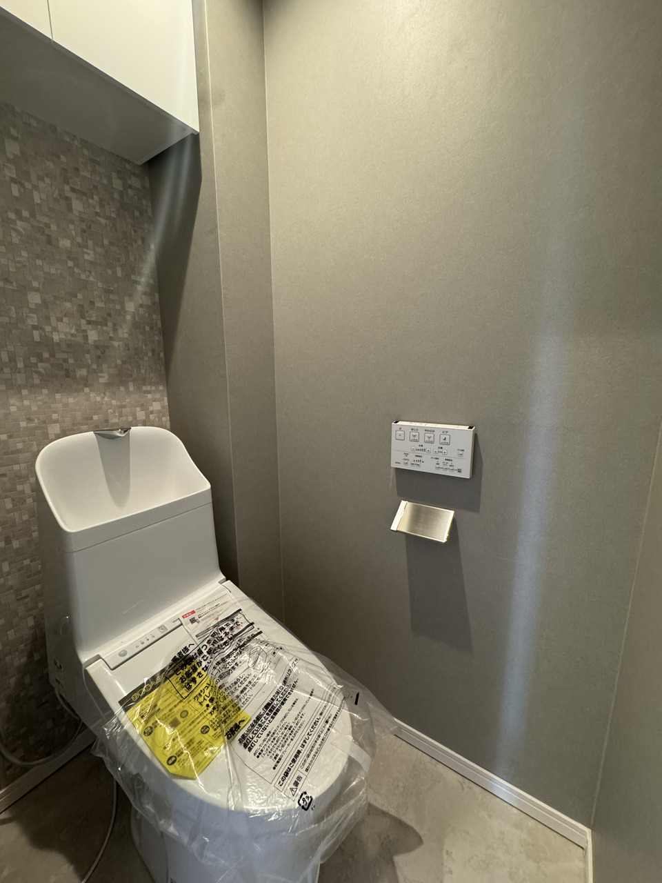 【トイレ】温水洗浄便座付きのトイレ。壁付けリモコンが設置されているので、操作がしやすいです。上部には吊戸棚があるため、ストック類をすっきりと収納可能です。